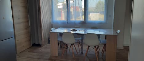 Un comedor con una mesa y sillas, una ventana con cortinas y piso de madera.
