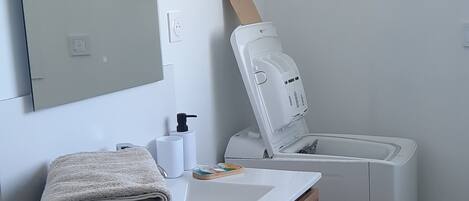 A bathroom with a wooden vanity, a white sink, a mirror, a towel stack, a soap dispenser, and a toilet.