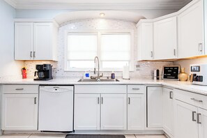 A modern kitchen with white cabinetry, a built-in dishwasher, a coffee maker, and a window above the sink. - Parkway Palace: 5BR Pet friendly home near downtown Sleeps 10 Game Room included (Louisville)