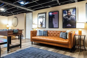 A room with a brown leather sofa, a foosball table, and posters on the wall. - Parkway Palace: 5BR Pet friendly home near downtown Sleeps 10 Game Room included (Louisville)