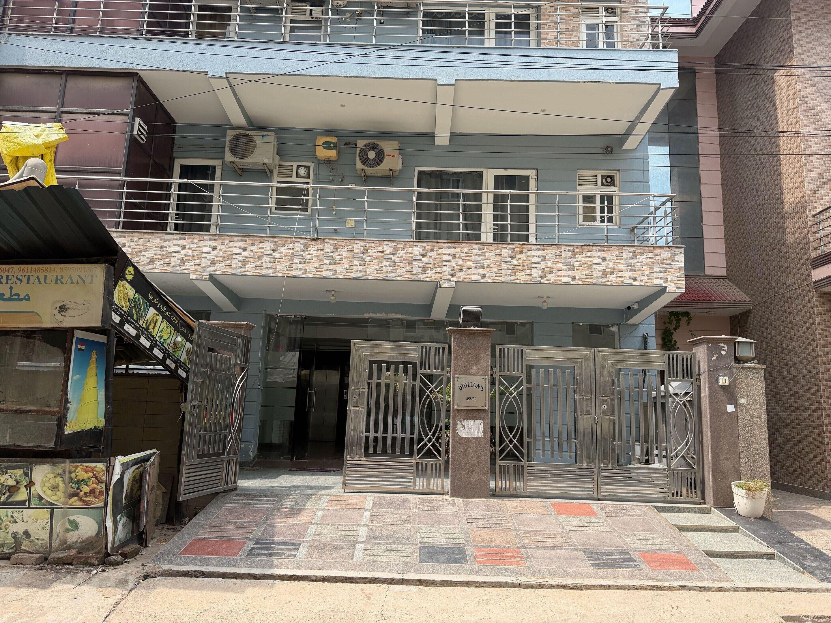 A building with a gated entrance, multiple air conditioning units, and a signboard with a phone number.