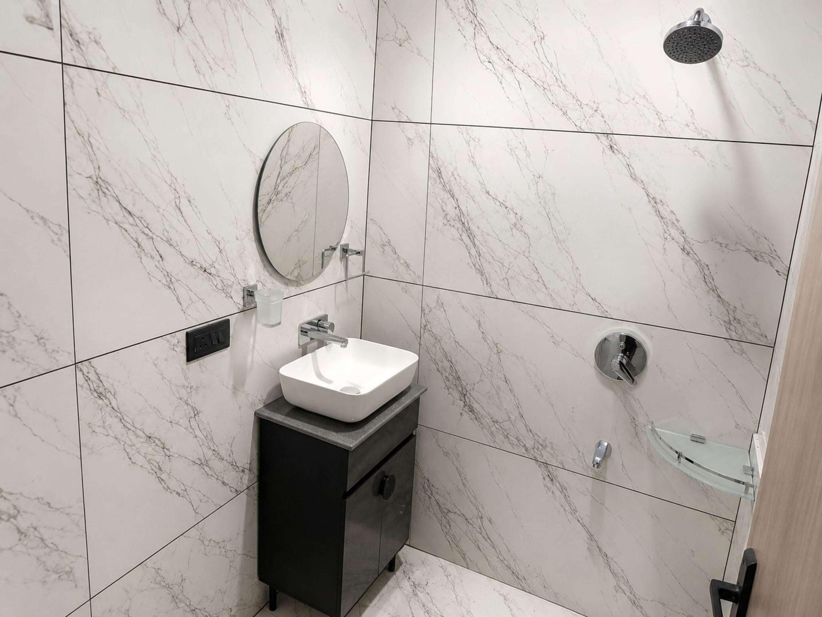 A bathroom with a white marble sink, a mirror, a shower, and a glass-enclosed sink vanity.