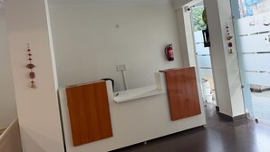 Een receptiebalie met een witte toonbank en houten panelen, een brandblusser aan de muur, en een uitzicht op buiten via een glazen deur.