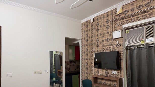 Een hotelkamer met een bed, een aan de muur bevestigde televisie, een klein tafeltje, twee stoelen en een badkamer zichtbaar door een open deur.