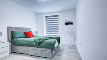 A bedroom with a bed, a nightstand, a wall-mounted fan, and a window with blinds.