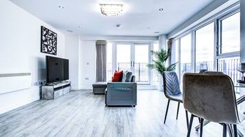 A modern living room with a flat-screen TV, grey sofa, dining table, and chairs.