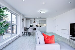 A modern living room with a white sofa, a dining area, and a kitchen in the background.