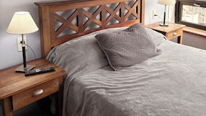 A bedroom with a wooden headboard, a grey bedspread, a pillow, a bedside lamp, and a remote control on a wooden nightstand. - Tango Apart en Avenida Corrientes (Buenos Aires)