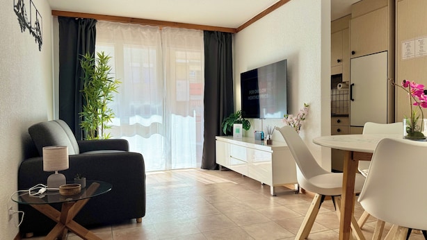 Un salon moderne comprenant un canapé, une table basse en verre, un téléviseur et un coin repas avec une table et des chaises blanches.
