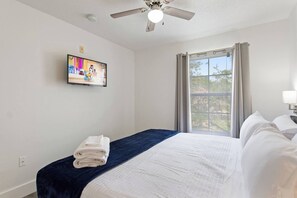 Ein Hotelzimmer mit Bett, Flachbildfernseher an der Wand, Deckenventilator und einem Fenster mit Vorhängen.