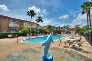 A swimming pool with lounge chairs and a dolphin statue, surrounded by buildings and palm trees. - Allure | Sleeps 8 | 3 BDM | Disney (Kissimmee)