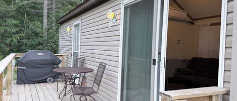 A covered deck with a grill, a table with chairs, and a sliding glass door leading to a room with a ceiling fan.