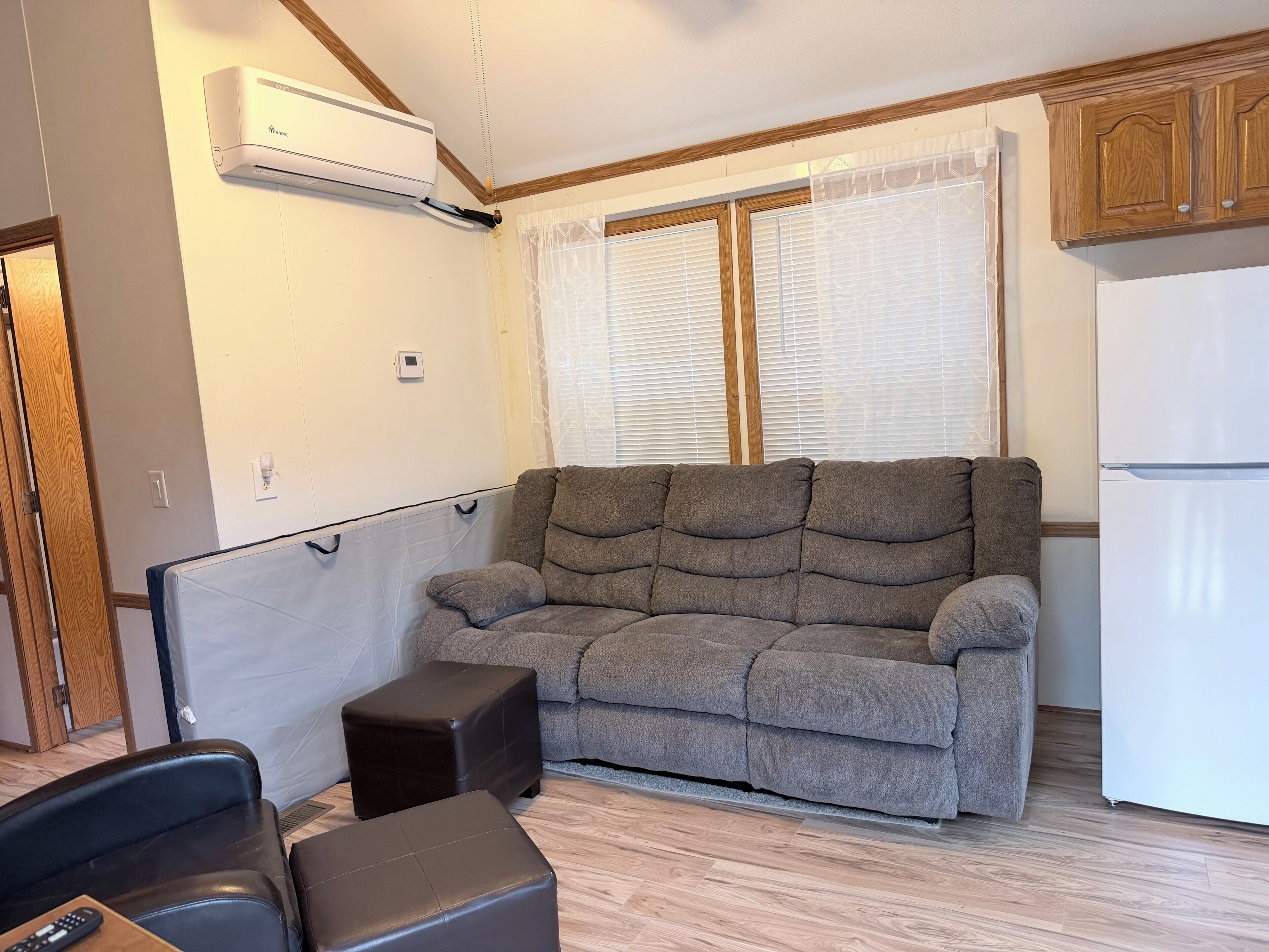 Un salon avec un canapé, un pouf et un réfrigérateur blanc.