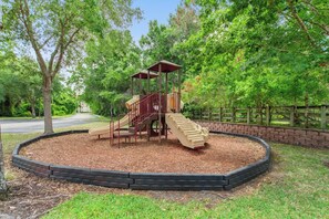 Ein Spielplatz mit Rutsche und Klettergerüst, umgeben von einer Ziegelmauer und Mulch.