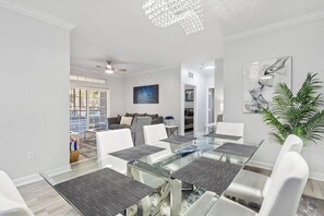 A modern dining area with a glass table, white chairs, and a ceiling fan. - Royale Blue | 3 BDM | Sleeps 8 | Disney | Resort (Davenport)