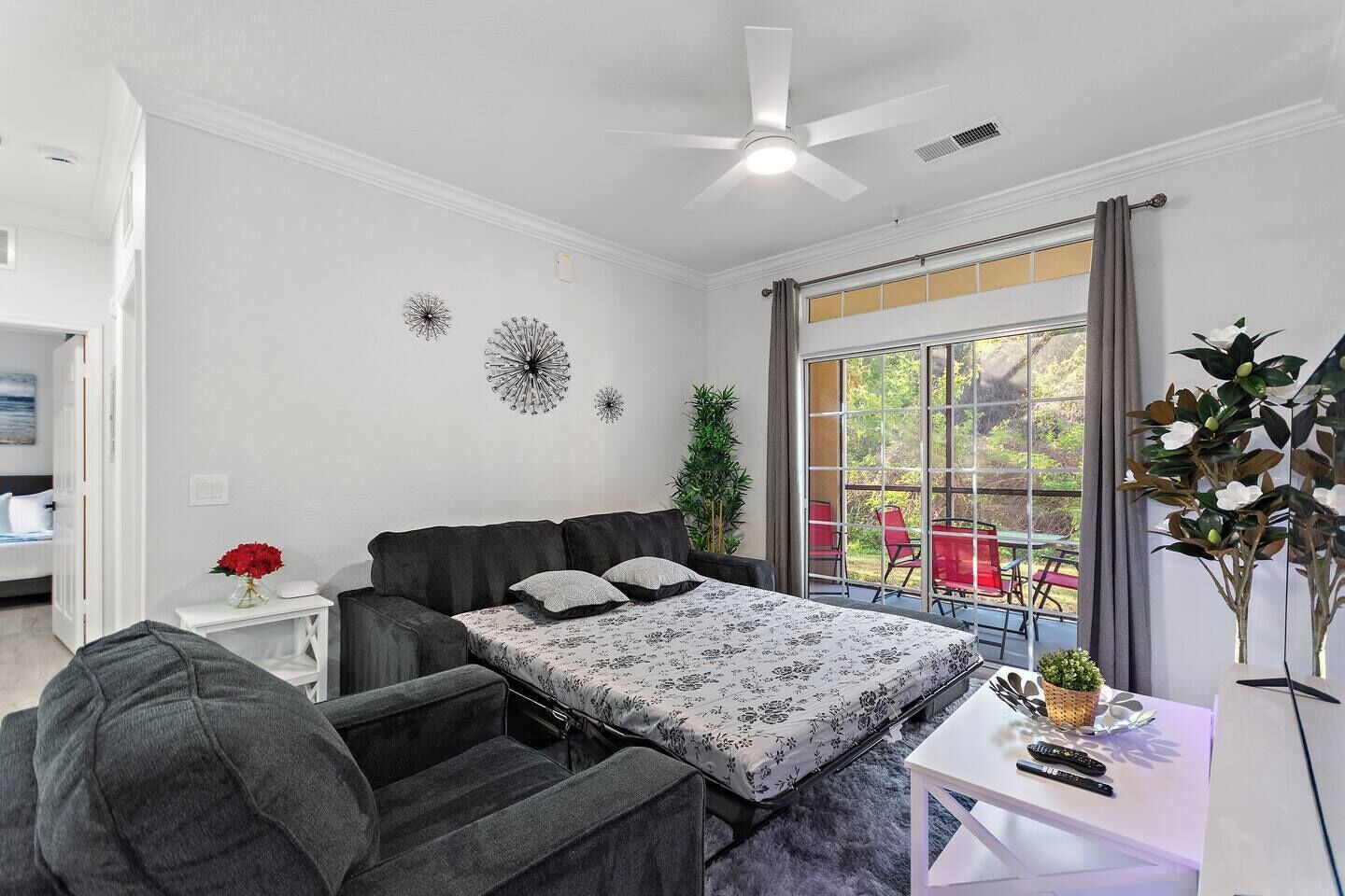Un dormitorio con cama, escritorio, silla, ventilador de techo y ventana con vista al exterior.