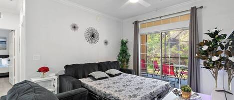 Un dormitorio con cama, escritorio, silla, ventilador de techo y ventana con vista al exterior.