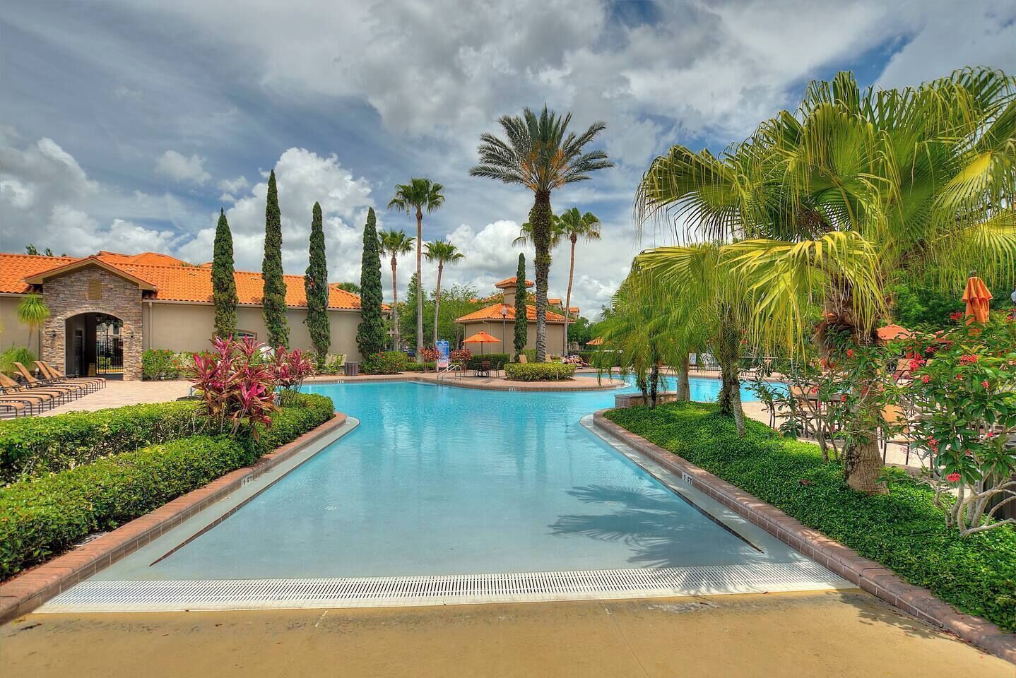 A swimming pool with surrounding palm trees and a building with a red-tiled roof.