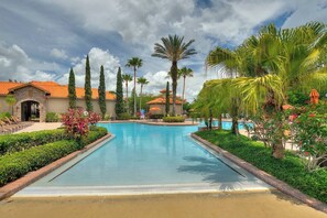 Ein Pool mit Palmen und ein Gebäude mit rotem Ziegeldach.