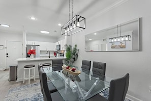 A modern kitchen with white cabinets, a stainless steel refrigerator, and a dining area with a glass table and black chairs. - Gentle Breeze | 3BDM | Sleeps 8 | Disney | Resort (Davenport)