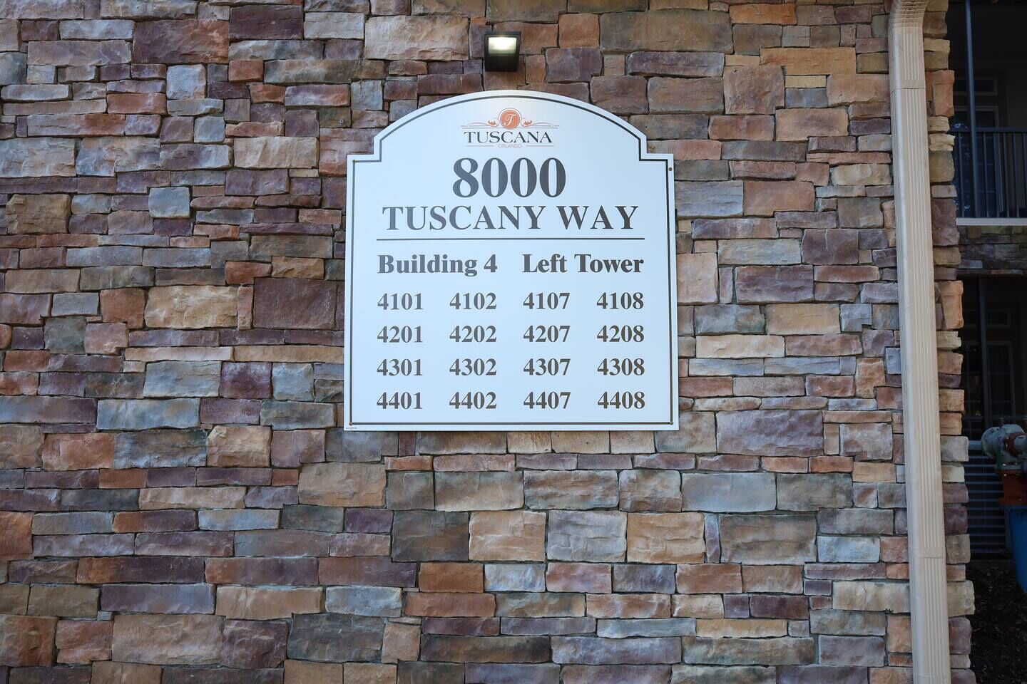 Un muro de piedra con un cartel que enumera los números de los edificios del Edificio 4 en Tuscany Way.