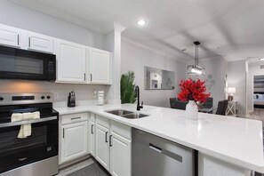 A modern kitchen with white cabinetry, stainless steel appliances, and a central island. - Gentle Breeze | 3BDM | Sleeps 8 | Disney | Resort (Davenport)