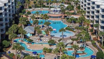 Um hotel com várias varandas, piscina central e palmeiras ao redor.