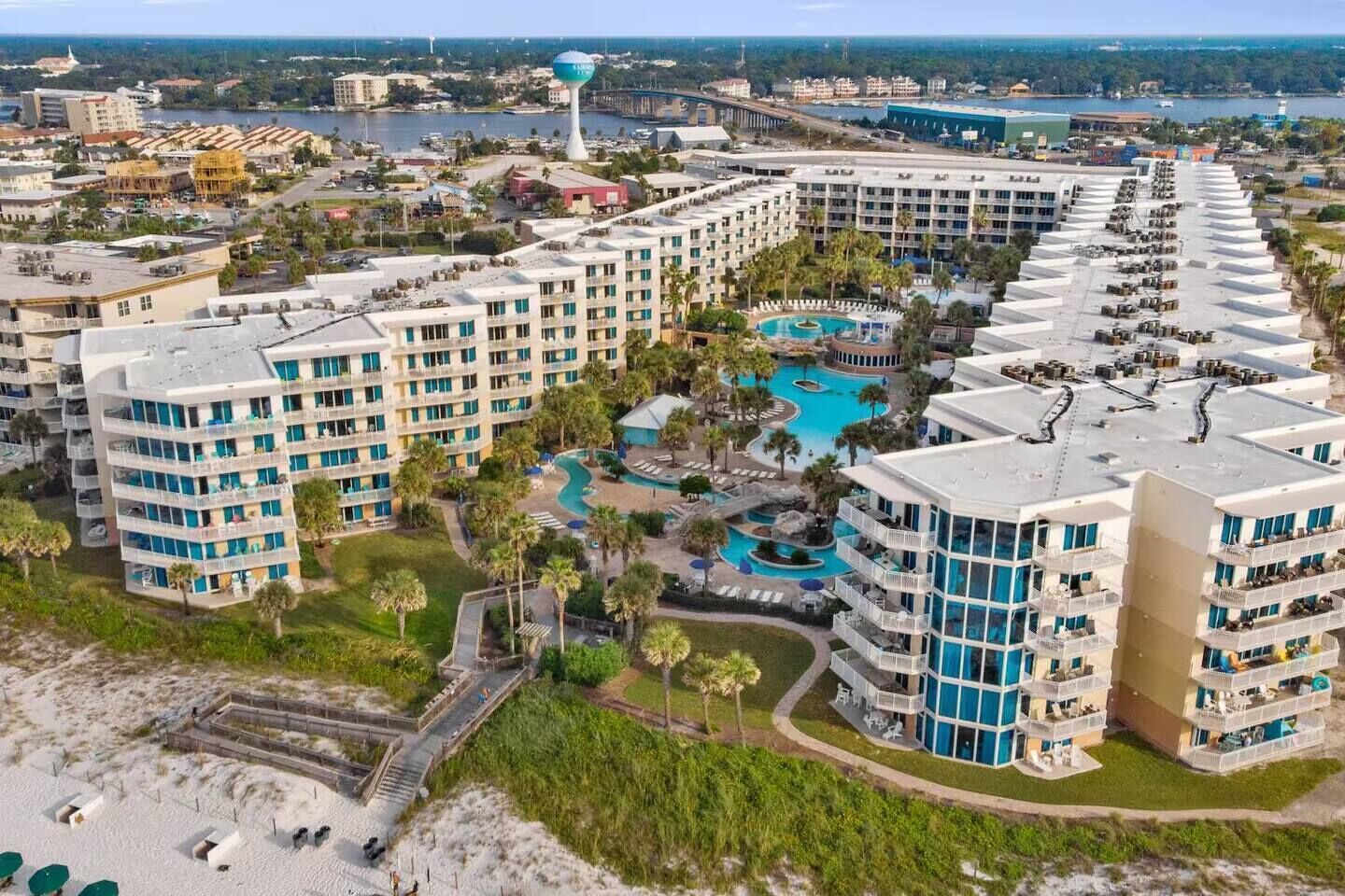 Resort com vários edifícios altos, piscina central e área de praia.