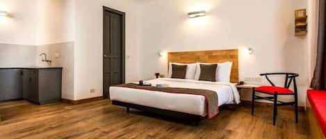A hotel room with a bed, bedside table, chair, and a kitchenette area.