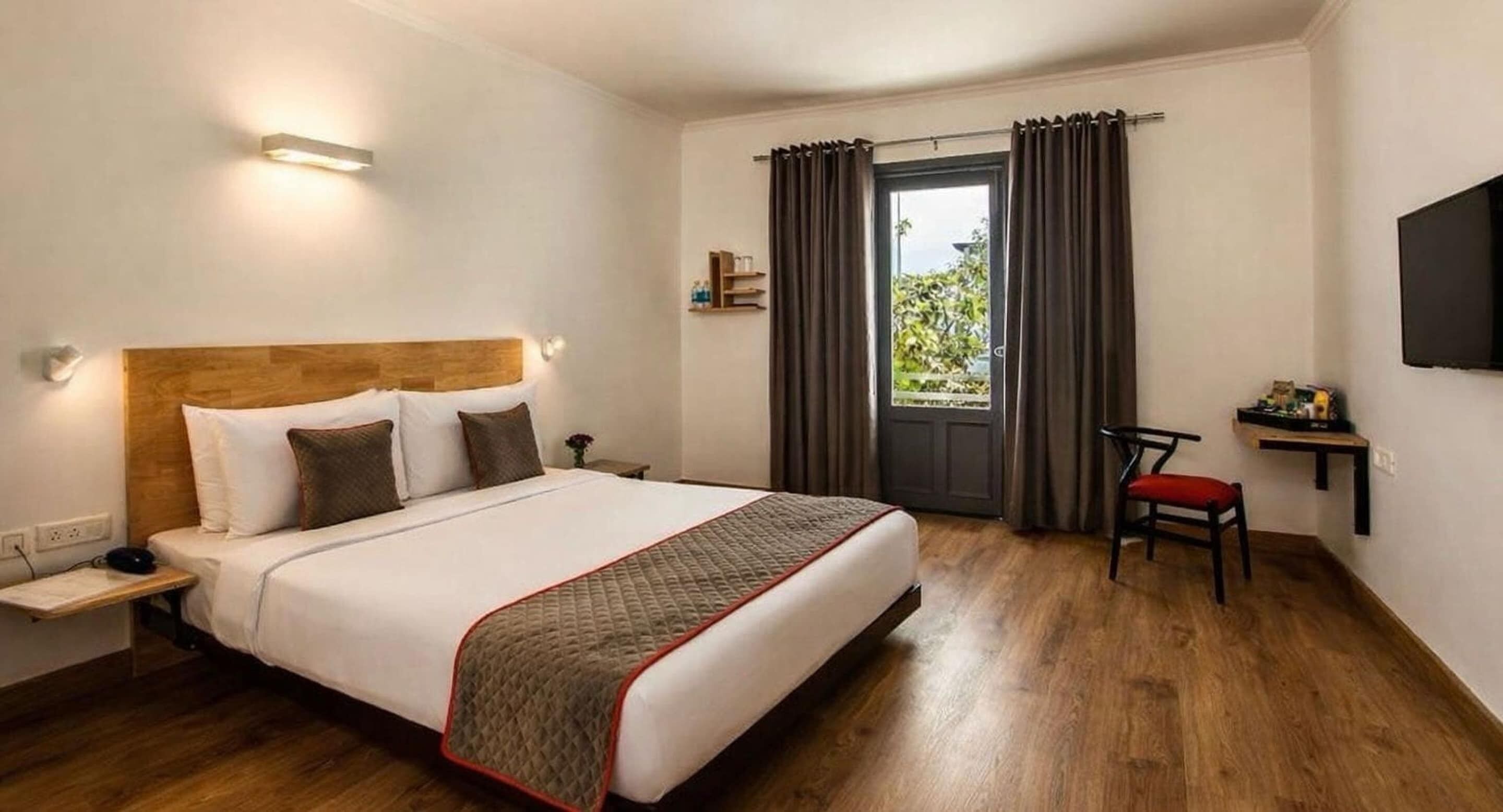 A hotel room with a bed, bedside table, chair, and a TV on the wall.
