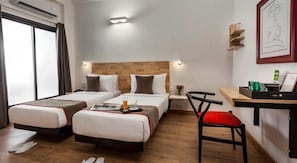 Una habitació d'hotel amb dos llits, una taula de treball, una cadira i una finestra.