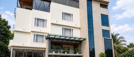 A multi-story building with a flat roof, large windows, and a balcony with potted plants.