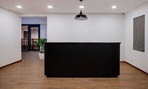 Tauleller de recepció en un interior modern amb sòl de fusta, un panell negre i una làmpada penjant.