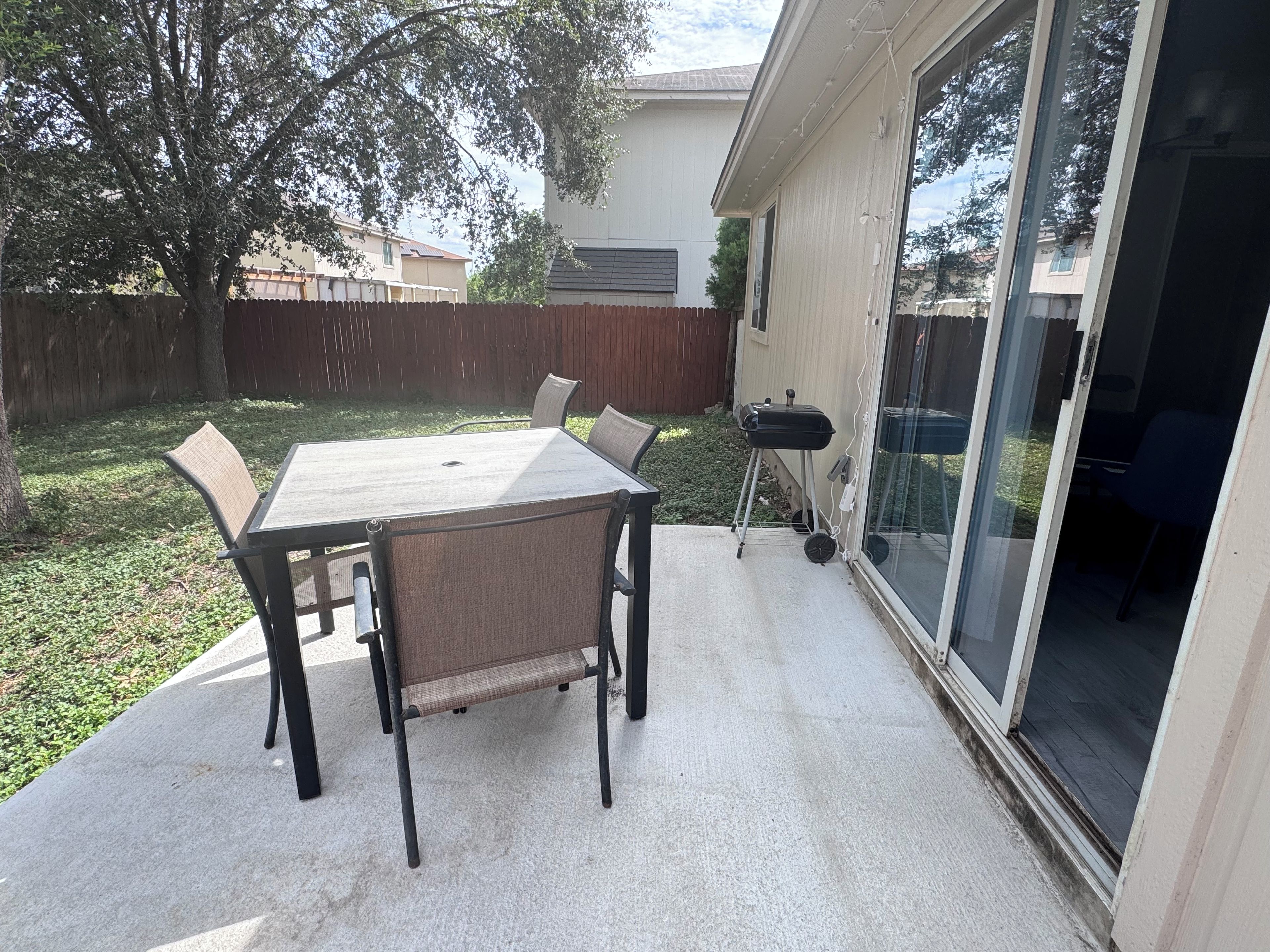 Un patio con mesa y sillas, una parrilla y un cerramiento de vidrio corredero que da a un espacio interior.
