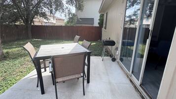 Un patio con mesa y sillas, una parrilla y un cerramiento de vidrio corredero que da a un espacio interior.