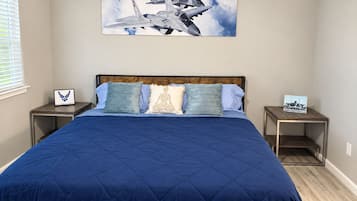 A bedroom with a large bed, a headboard, two bedside tables, and a wall-mounted picture of fighter jets.
