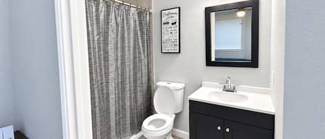 A modern bathroom with a shower curtain, toilet, sink, and mirror.