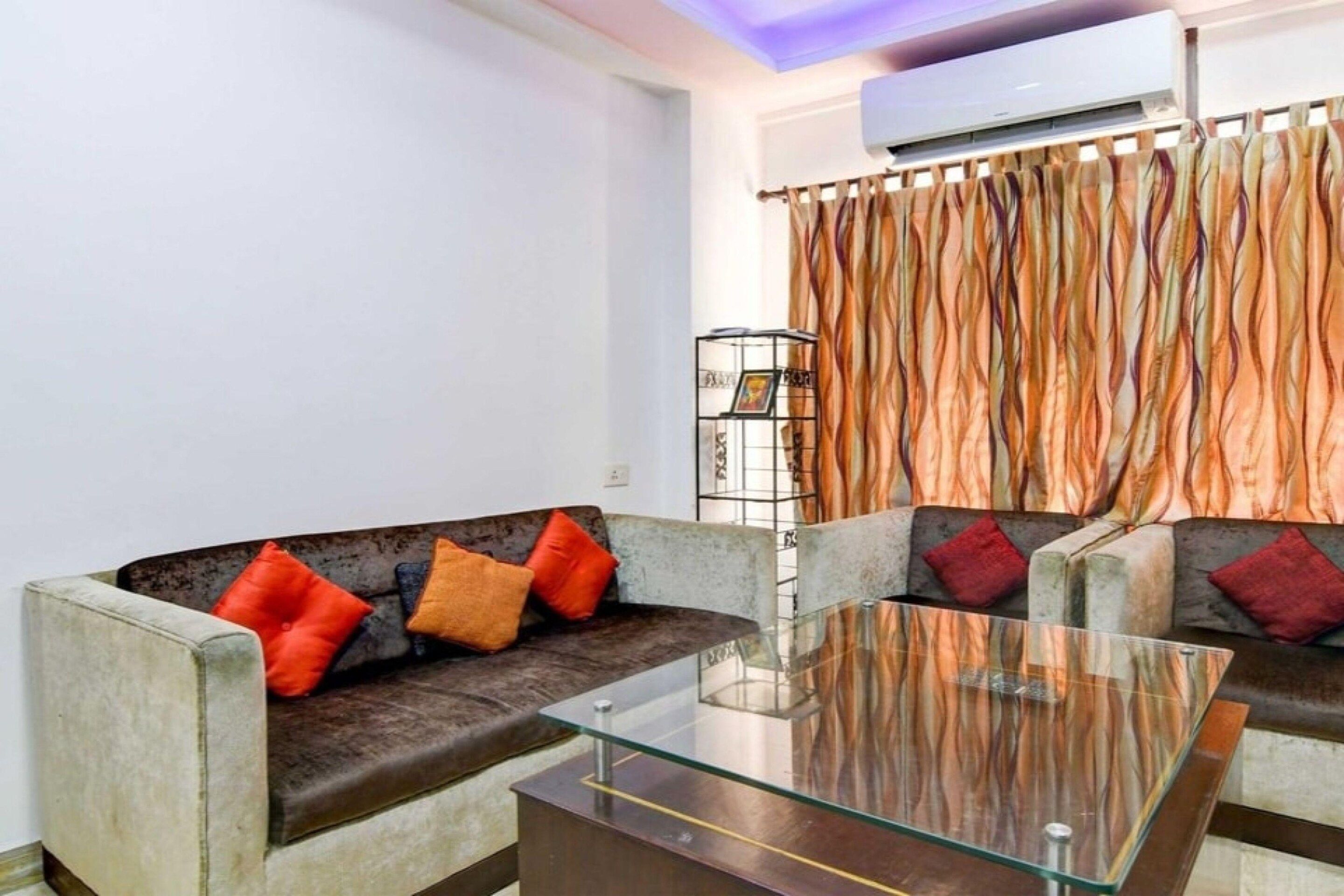 Ein Wohnzimmer mit einer Couch, Kissen, einem Glastisch und einem gemusterten Vorhang.