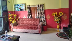 A living room with a sofa, a television mounted on the wall, and a red and yellow wall design.