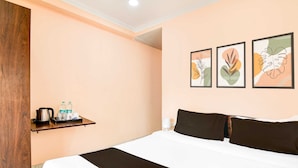 A hotel room with a bed, a shelf with toiletries, and three framed artworks on the wall.