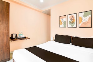 A hotel room with a bed, a shelf with toiletries, and three framed artworks on the wall. - Classic Murshidabad Junction (Lalbag)