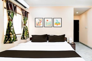 A hotel room with a bed, curtains, a nightstand, a lamp, and three framed artworks on the wall.