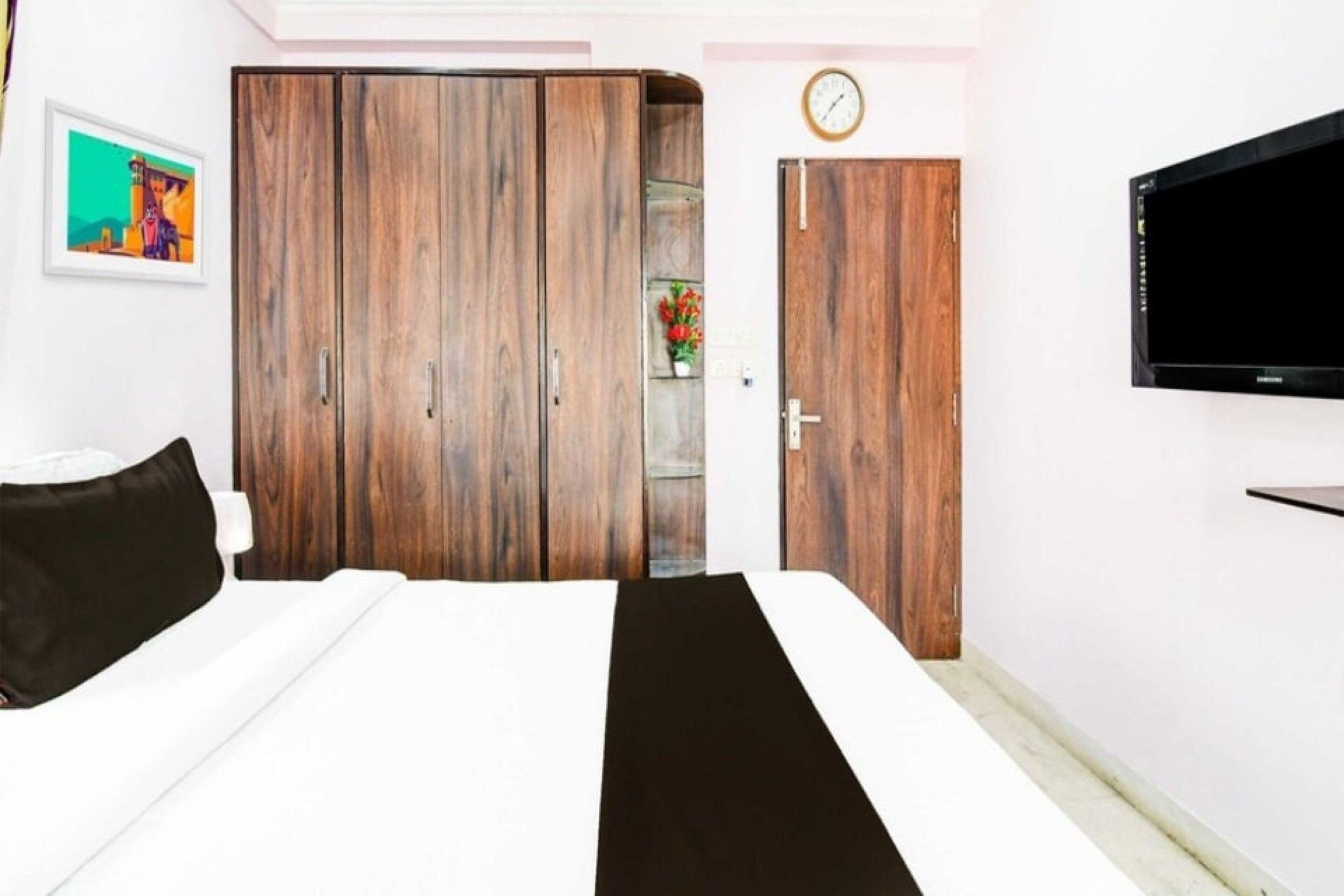 A bedroom with a bed, a wardrobe, a TV, and a clock on the wall.