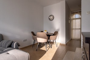 A dining area with a round table and four chairs, a clock on the wall, and a sofa in the foreground. - 3BR Sunset View Retreat Steps from the Beach (Oroklini)
