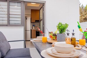 A modern kitchen with a dining area, featuring a table set with plates, bowls, and glasses of orange juice. - Modern 2BR Coastal Escape 100m from Sea (Voroklini)