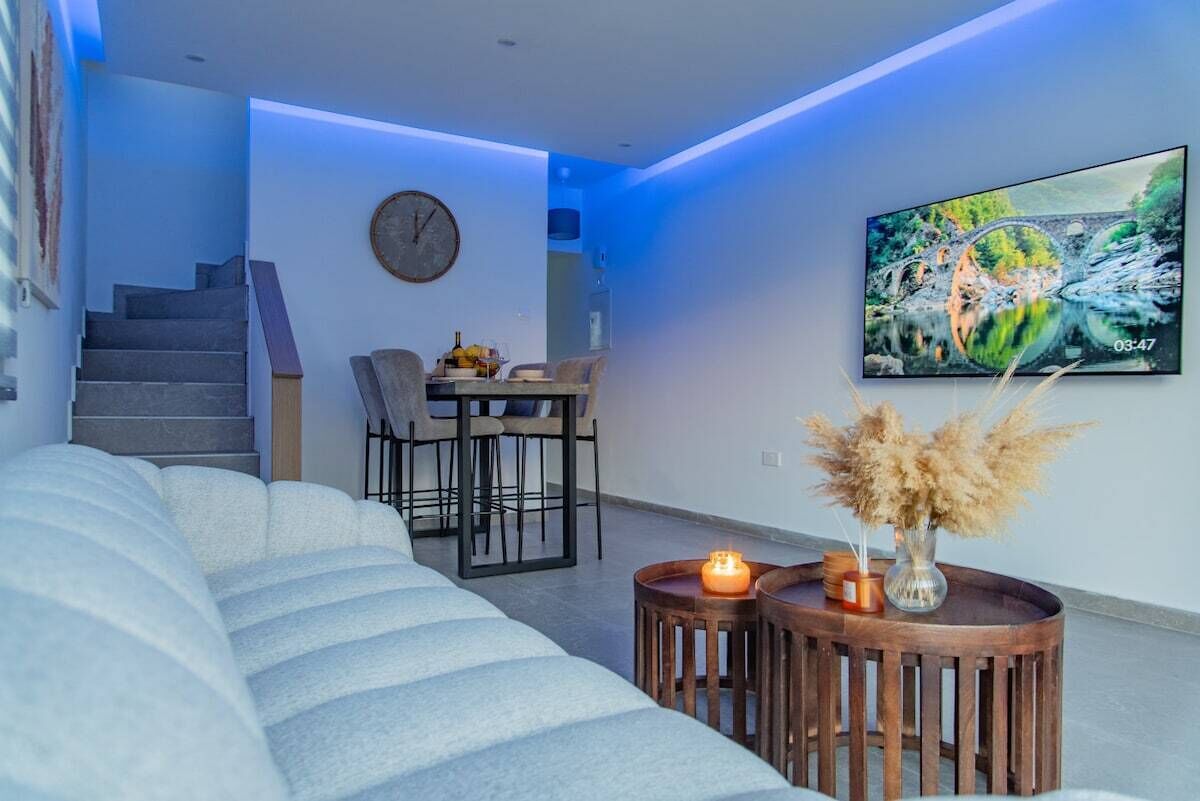 Ein modernes Wohnzimmer mit einer Couch, einem Essbereich mit Stühlen, einem Fernseher an der Wand und einer Uhr.