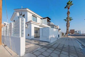 A modern two-story house with a white exterior, a gated entrance, and a palm tree in the background. - Modern 2BR Coastal Escape 100m from Sea (Voroklini)