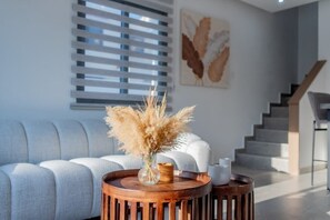 A modern living room with a grey sofa, a wooden coffee table with a vase of dried flowers, and a staircase in the background. - Modern 2BR Coastal Escape 100m from Sea (Voroklini)