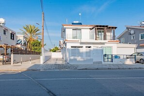 A residential street with a two-story house featuring a balcony, a garage, and a car parked in front. - Modern 2BR Coastal Escape 100m from Sea (Voroklini)