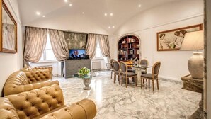 A spacious living room with a marble floor, a leather sofa, a dining area with chairs, a television, and a bookshelf. - CRISPI HOLIDAY IN (Roma)